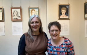 Two women smiling with arms around one another in an art gallery 