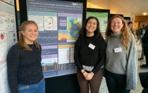 Three Oxford volcanology students standing beside poster